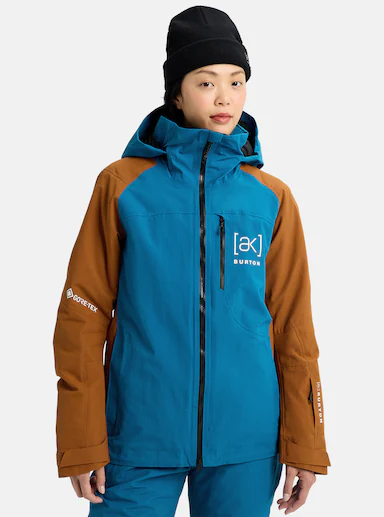Person wearing a blue and brown Burton jacket with the [ak] logo, featuring GORE-TEX on the sleeve. They have a black beanie and a neutral expression.