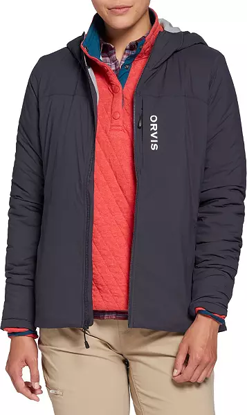 A person wears a dark gray hooded jacket with "ORVIS" written on it, over a red quilted pullover and plaid shirt. They have beige pants, creating a casual, layered look.