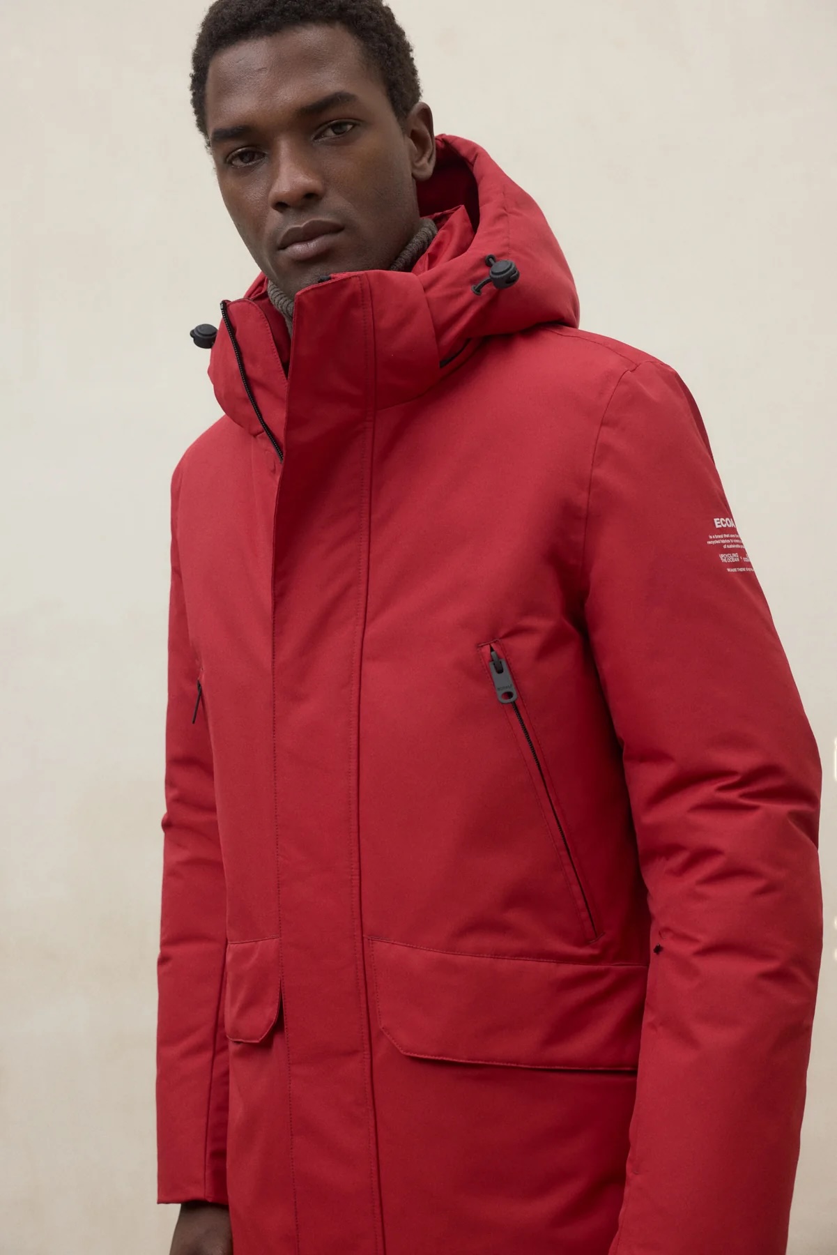 Man wearing a stylish red parka with a high collar and hood, looking confidently at the camera against a neutral background.